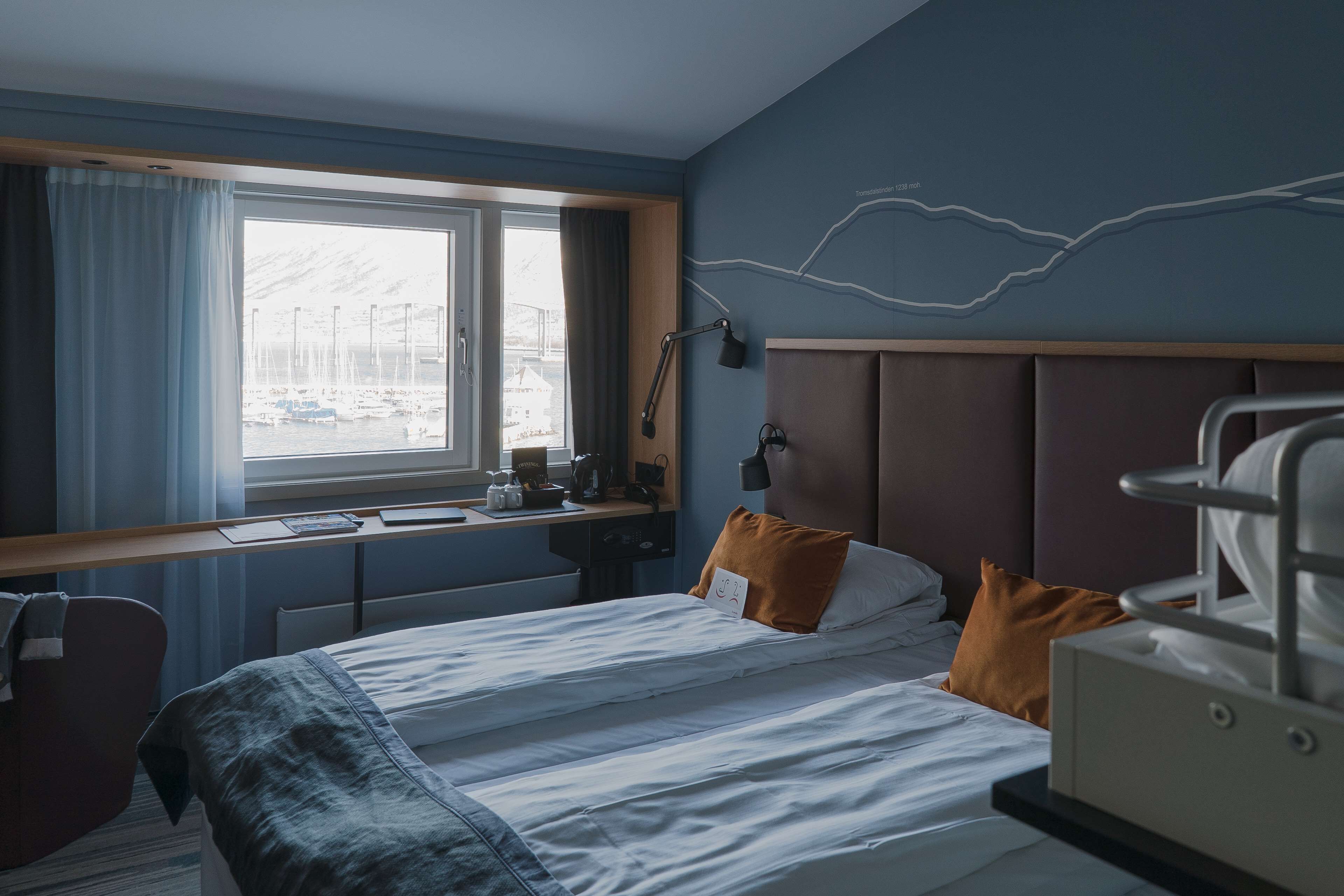 Une chambre d’hôtel avec un lit, un bureau, une chaise, une fenêtre donnant sur le port et un mur décoré d’un motif représentant un éclair.