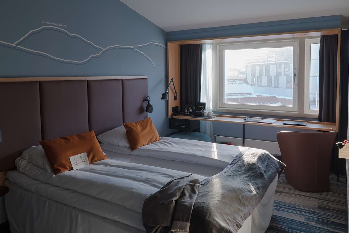 A hotel room with a large bed, a desk, and a window with curtains.