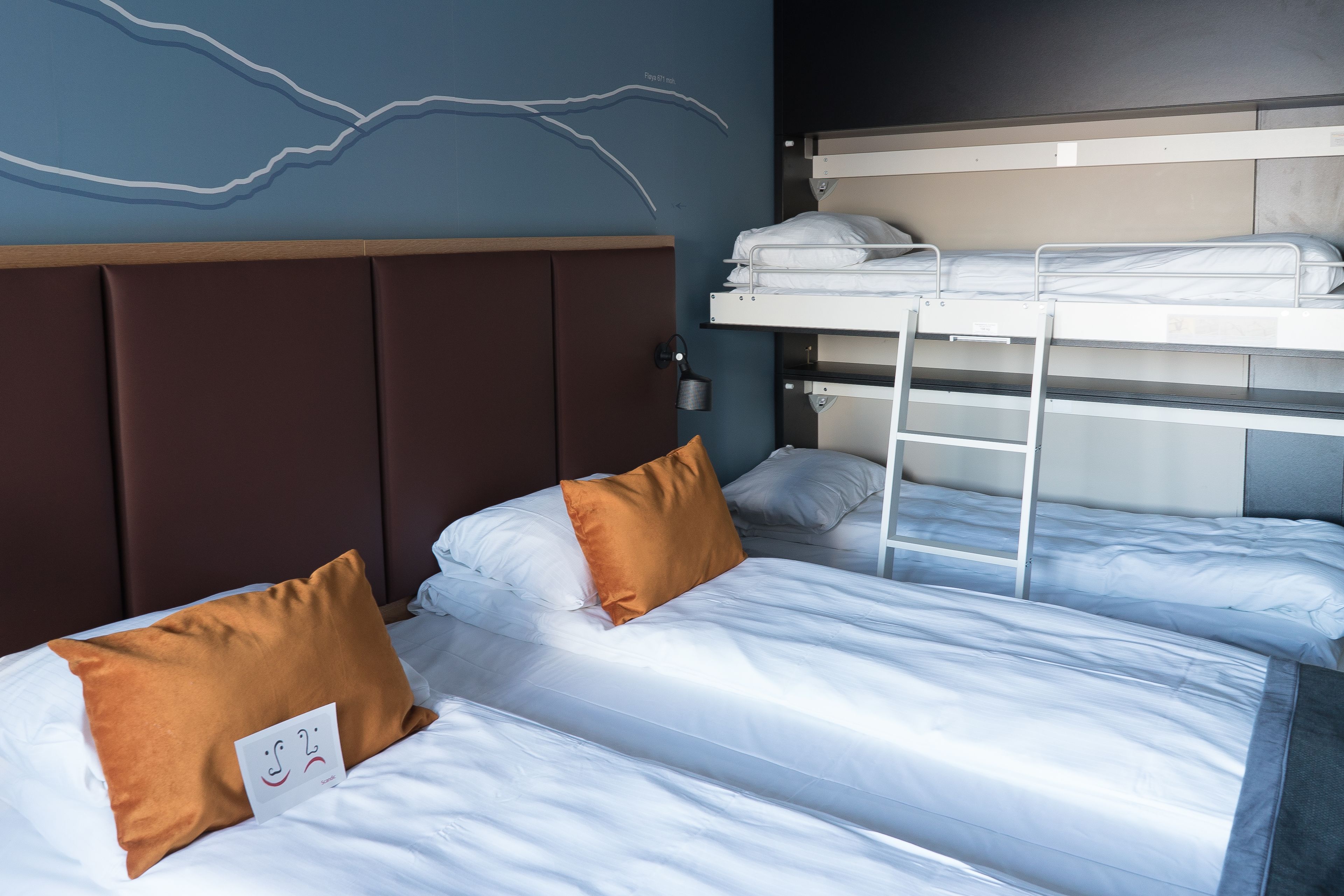 Ein Hotelzimmer mit zwei Einzelbetten, einem Etagenbett und einem Kopfteil mit Wellenmuster.