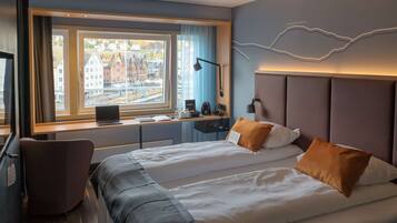 A hotel room with a large bed, a desk with a laptop, and a view of buildings outside the window.