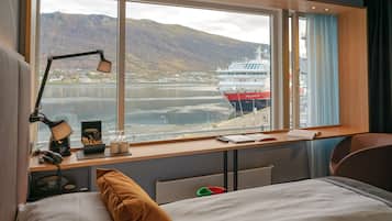 Een hotelkamer met een groot raam, met uitzicht op een schip en bergen.