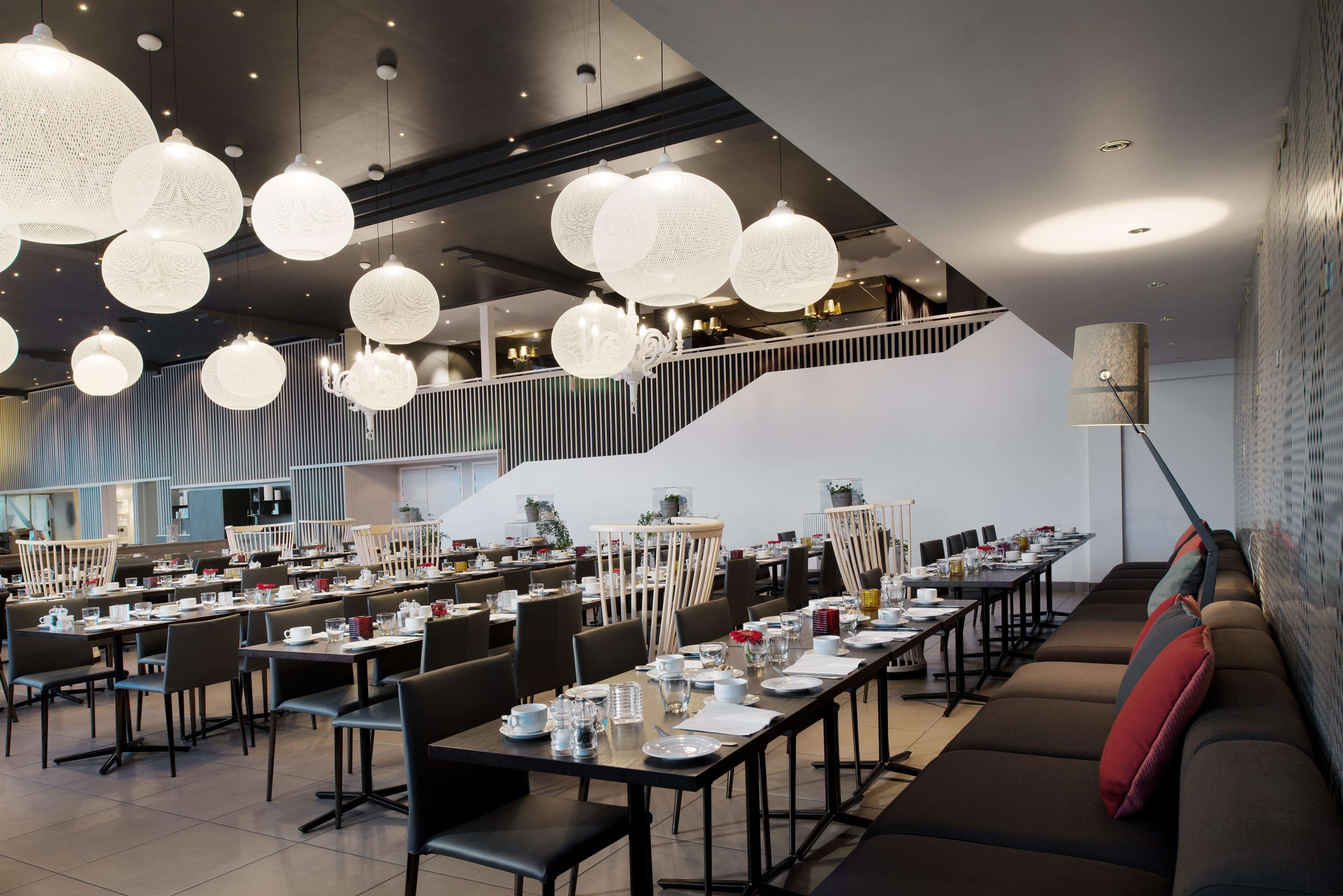 A modern dining area with multiple tables, chairs, and hanging spherical light fixtures.