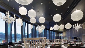 A modern dining area with multiple tables and chairs, large windows offering a view of snow-capped mountains, and decorative spherical light fixtures hanging from the ceiling. - Scandic Ishavshotel (Tromsø)