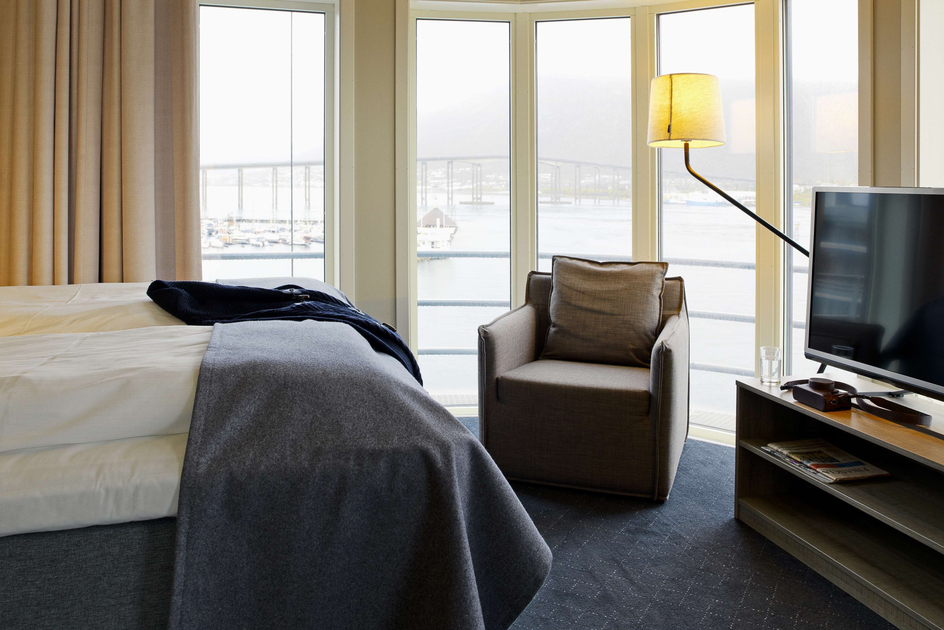 A hotel room with a bed, a chair, a TV, and a view of a bridge and water.