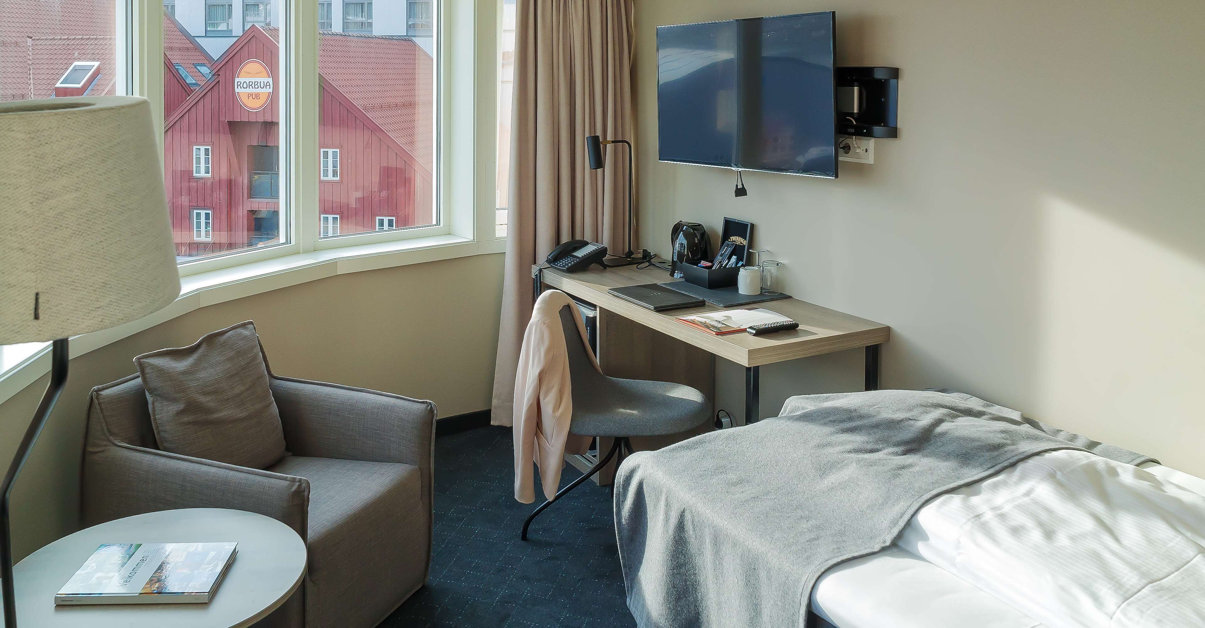 Une chambre d’hôtel avec un lit, un bureau avec un ordinateur, une chaise, une petite table et un téléviseur fixé au mur.