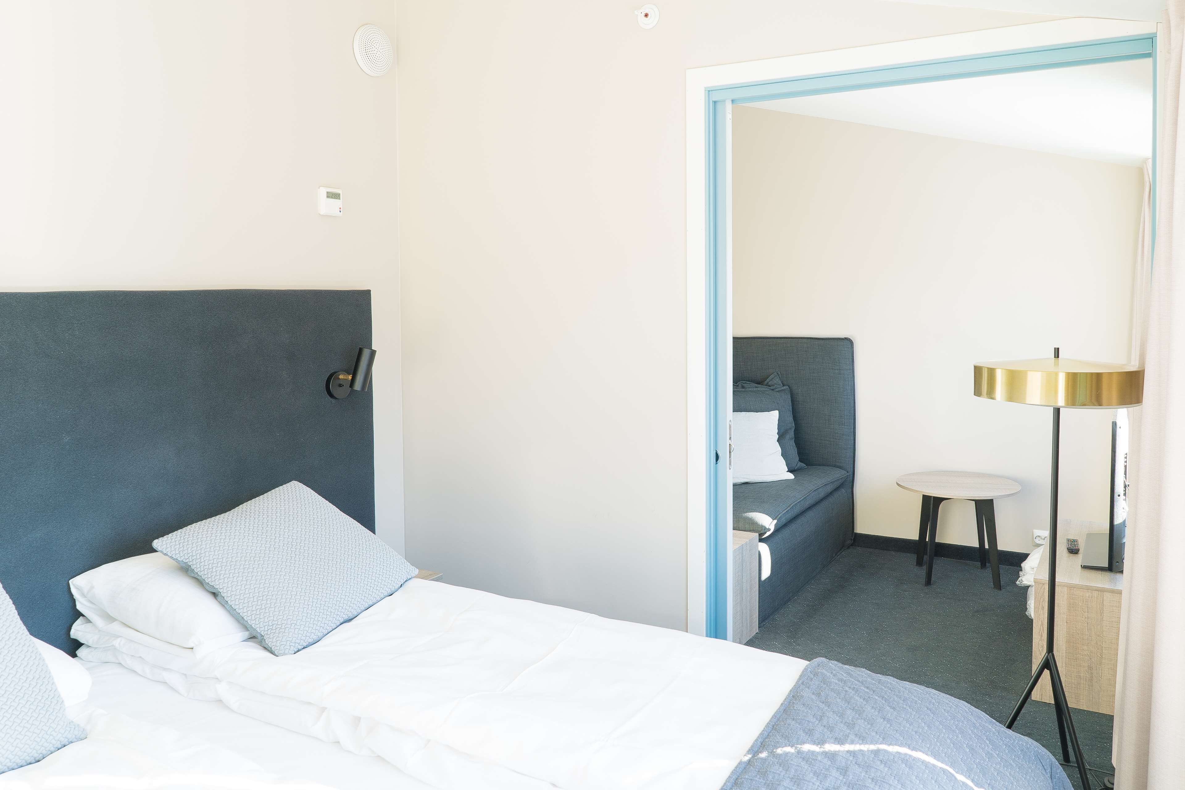 A hotel room with a bed, bedside table, lamp, and a small table with a chair.