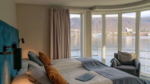 A bedroom with a large bed, a laptop, and a chair by the window overlooking a body of water and mountains. - Scandic Ishavshotel (Tromsø)
