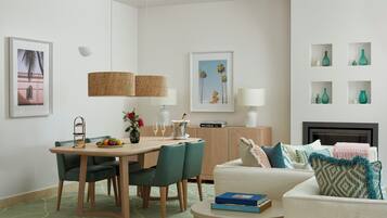 A modern living room with a dining area, featuring a wooden table, green chairs, a white sofa, and a fireplace.
