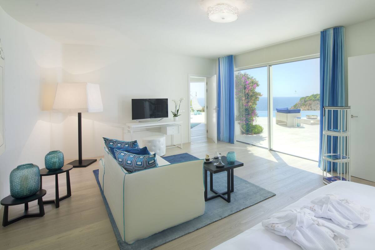 Een moderne hotelkamer met een groot bed, een bank, een televisie en een balkon met uitzicht op zee.