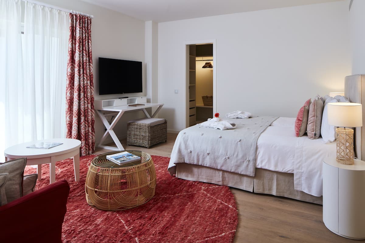 Een hotelkamer met een bed, een televisie, een bureau, een stoel, een rood vloerkleed en een rieten bijzettafeltje.