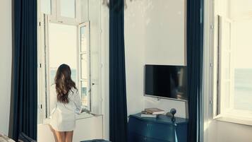Une chambre avec un grand lit, une télévision, un bureau et une vue sur la mer.