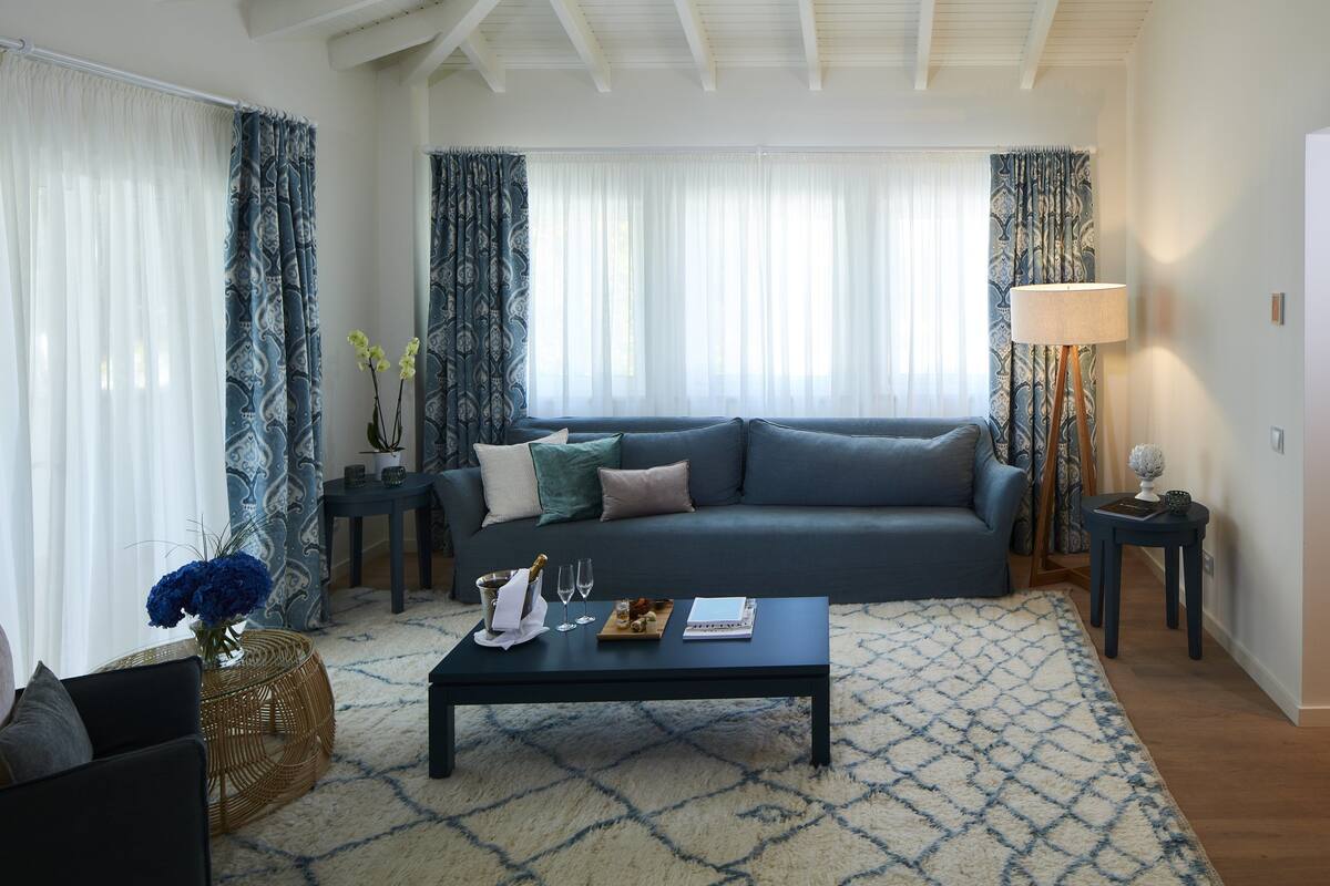 Een woonkamer met een donkerblauwe bank, een bijzettafeltje met een dienblad vol lekkernijen, een vaas met bloemen en een lamp op een salontafel.