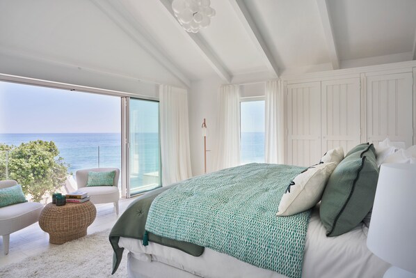 A bedroom with a large bed, a view of the sea, and a balcony with a chair.