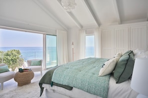 A bedroom with a large bed, a view of the sea, and a balcony with seating.