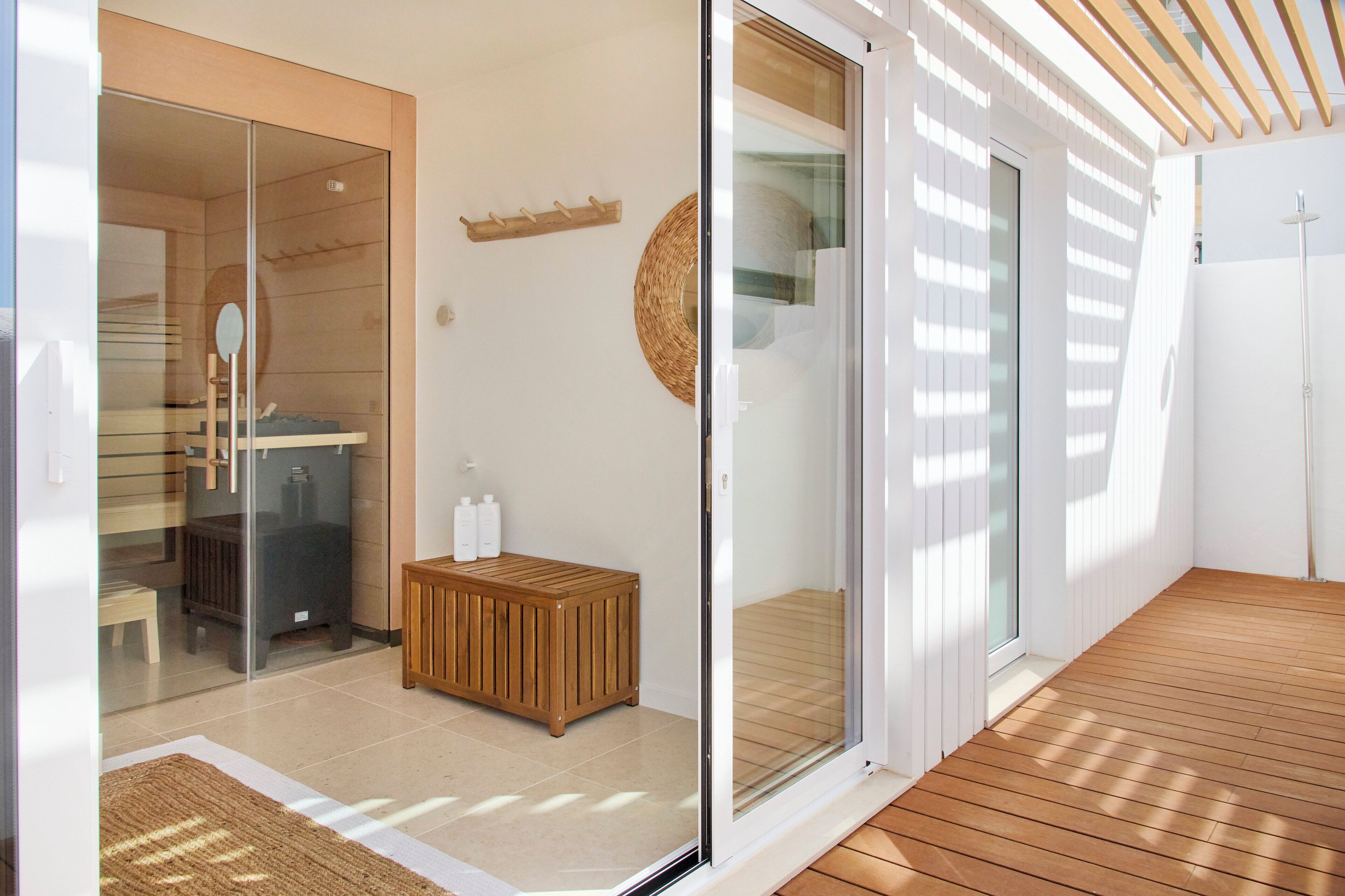 A modern bathroom with a glass shower enclosure, a wooden bench, and a towel rack.