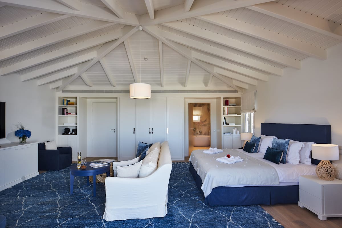 Een ruime slaapkamer met een hoge plafond, een groot bed, een witte bank en een klein tafeltje.