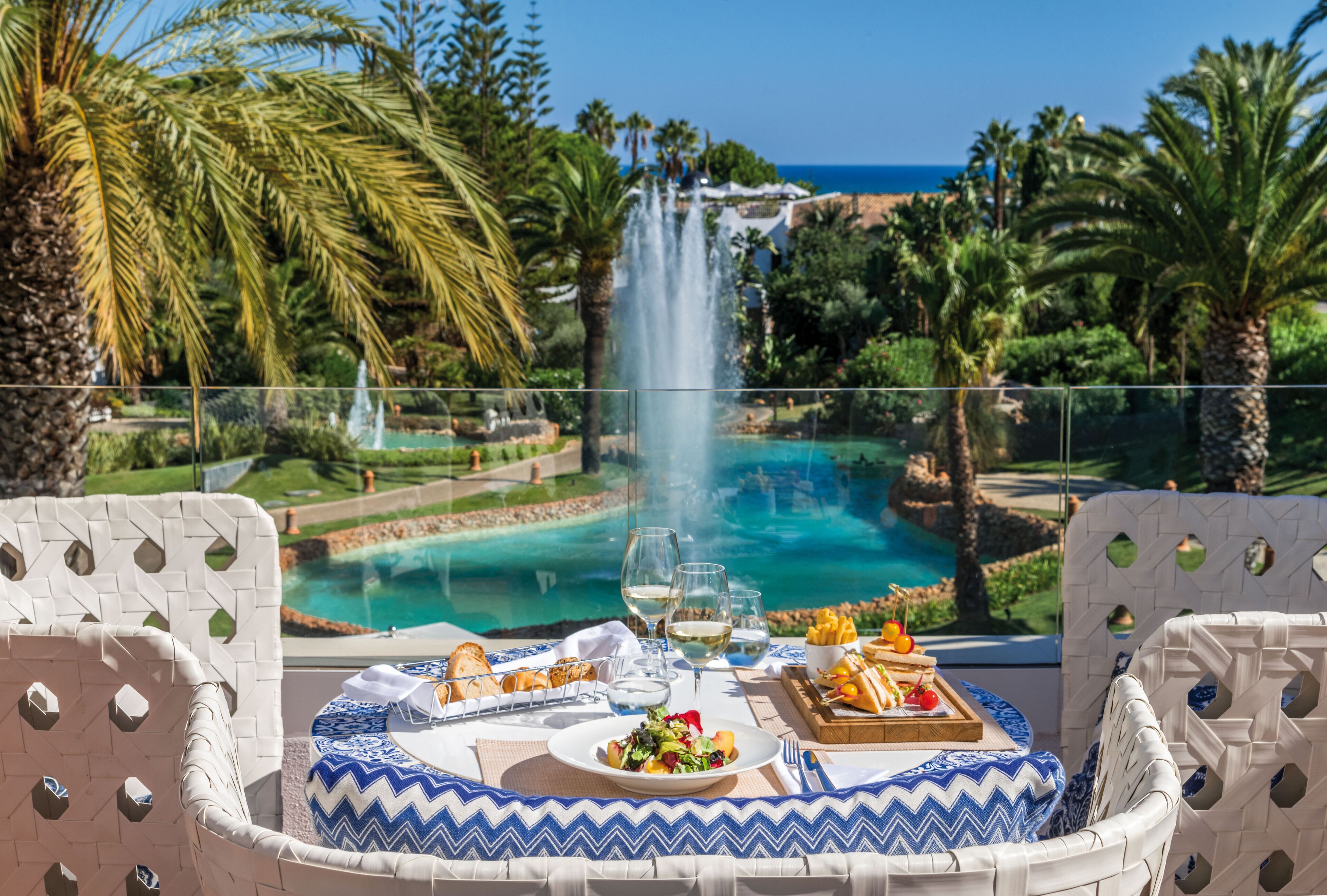 A dining area with a table set for two, overlooking a pool and a waterfall.