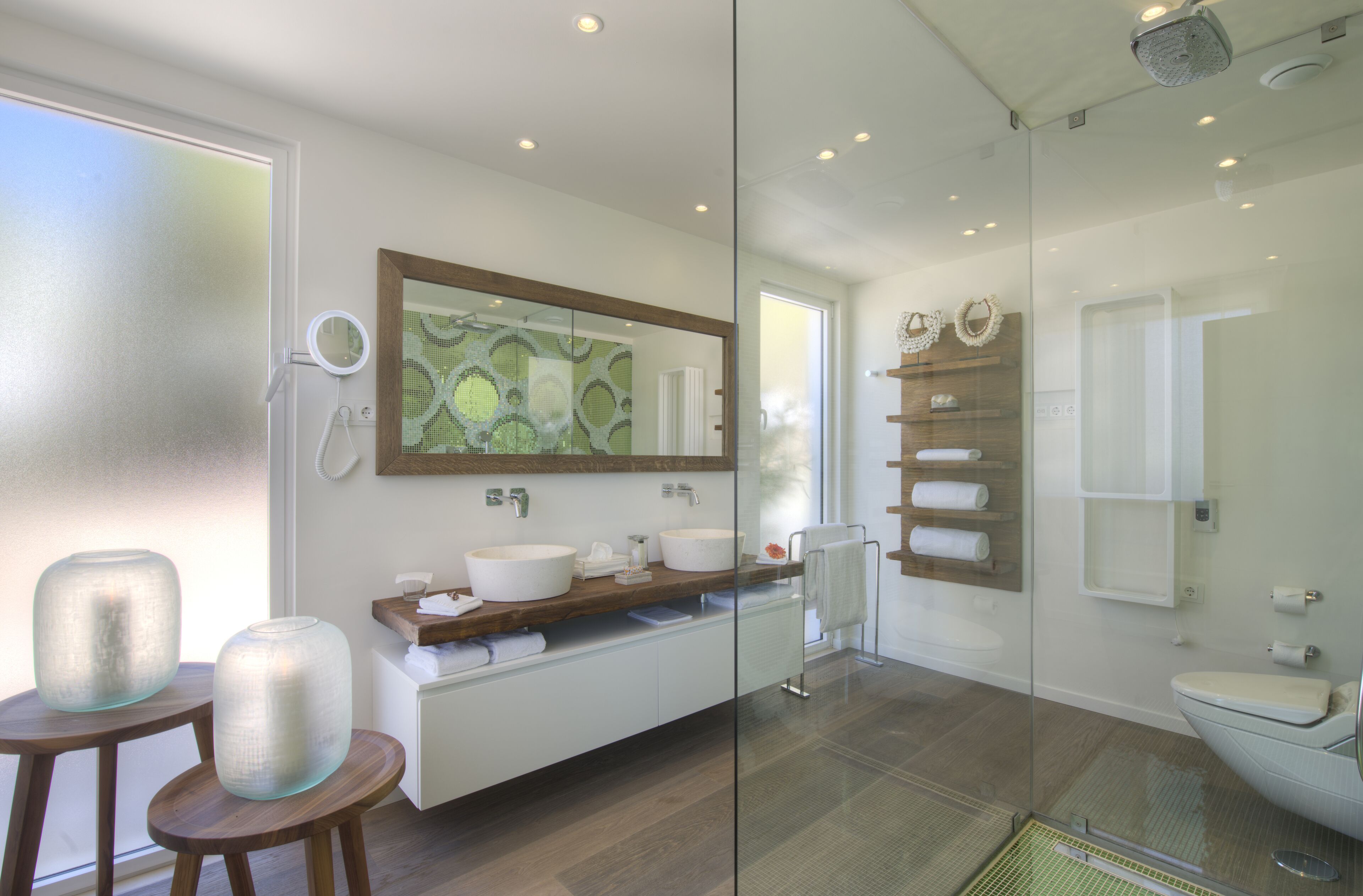 Ein modernes Badezimmer mit einer Glasdusche, einem großen Spiegel und einem Holzlager mit zwei Waschbecken.
