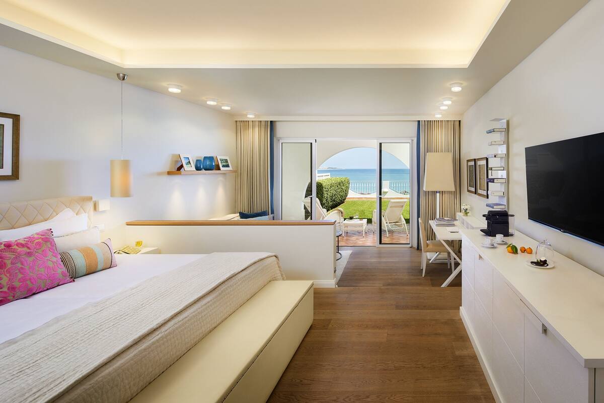 Een moderne hotelkamer met een bed, een bureau, een televisie en uitzicht op zee.