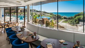 A restaurant with a view of a pool and ocean. Tables are set with plates and glasses.