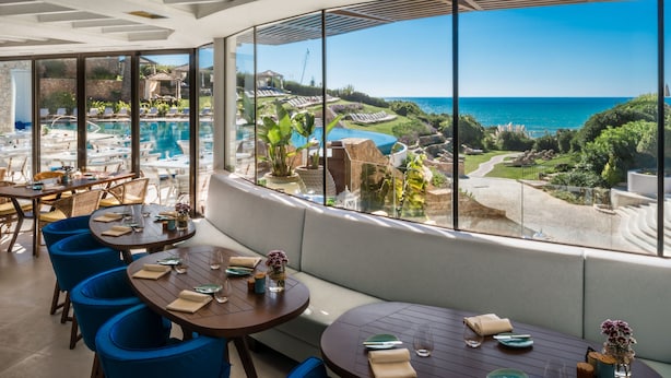 A restaurant with a view of a pool and ocean. Tables are set with plates and glasses. - Vila Vita Parc  (Lagoa)