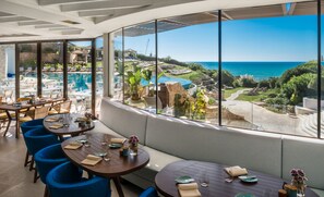 A restaurant with a view of a pool and ocean. Tables are set with plates and glasses.