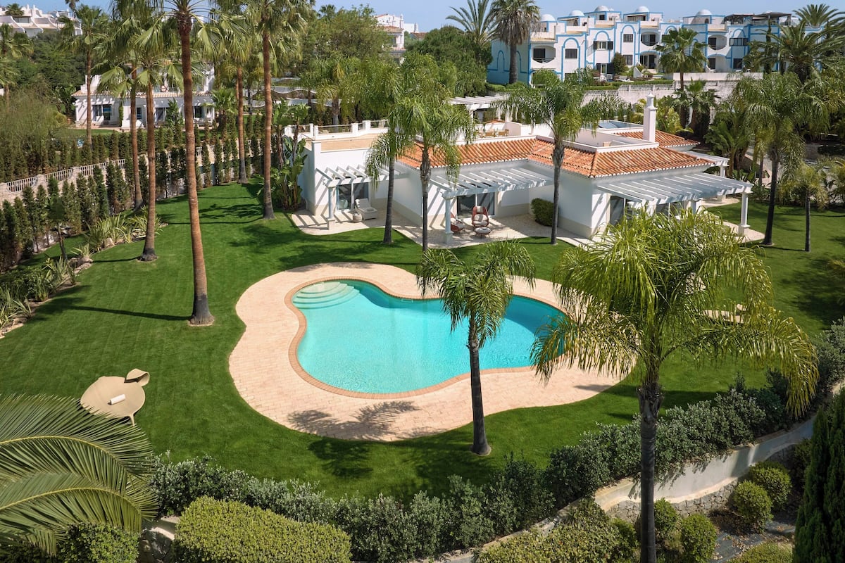 Een resort met een zwembad, palmbomen en een wit gebouw met een dak van rode tegels.