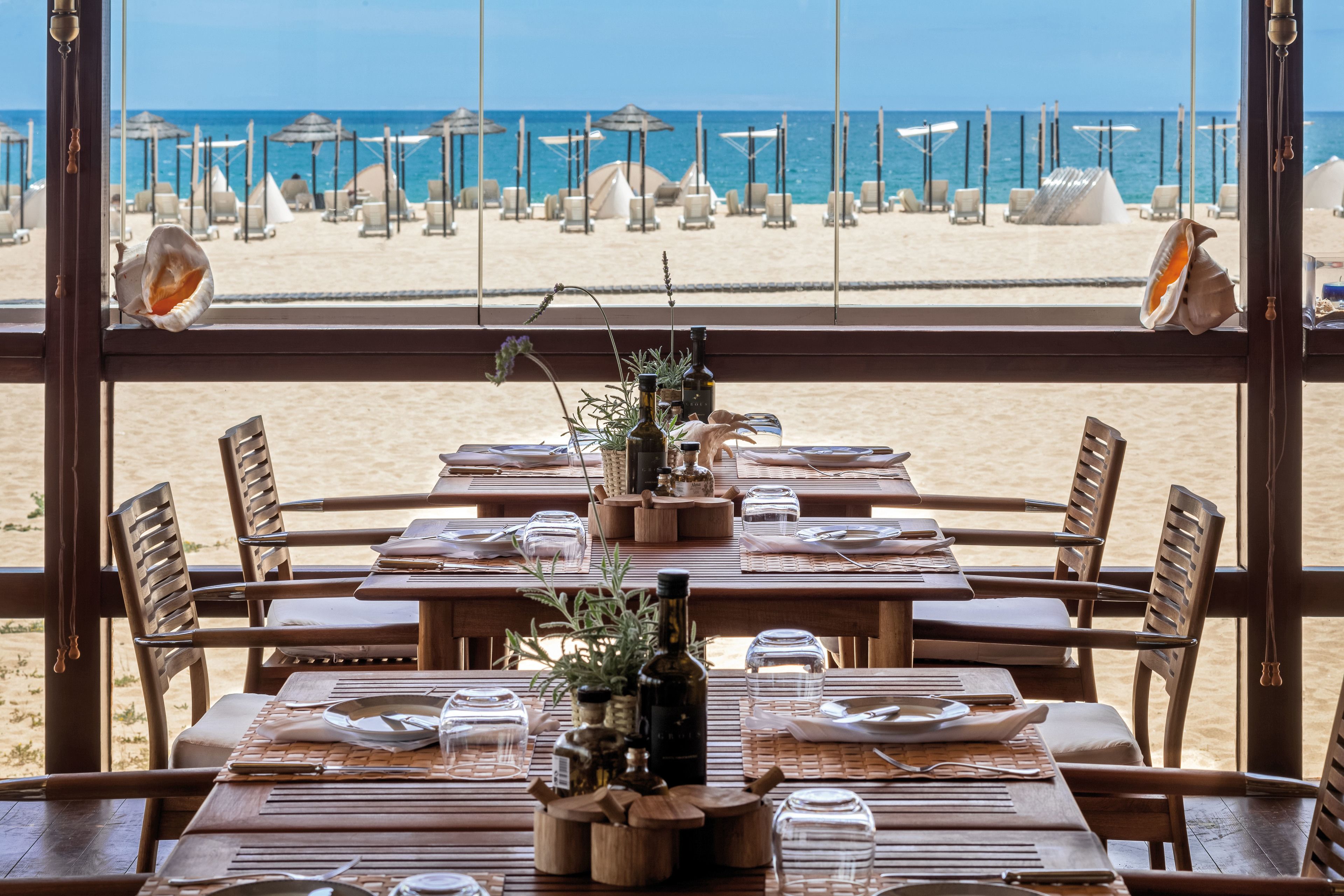 Un restaurante frente a la playa con mesas y sillas de madera, con vista a la playa y al océano.