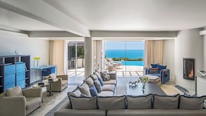 A modern living room with a large sofa, a coffee table, and a TV. There is a fireplace and a view of the ocean. - Vila Vita Parc  (Lagoa)