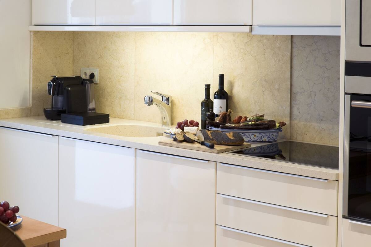 Een moderne keuken met witte kasten, een inbouwoven, een koffieapparaat en een fles wijn op het aanrecht.