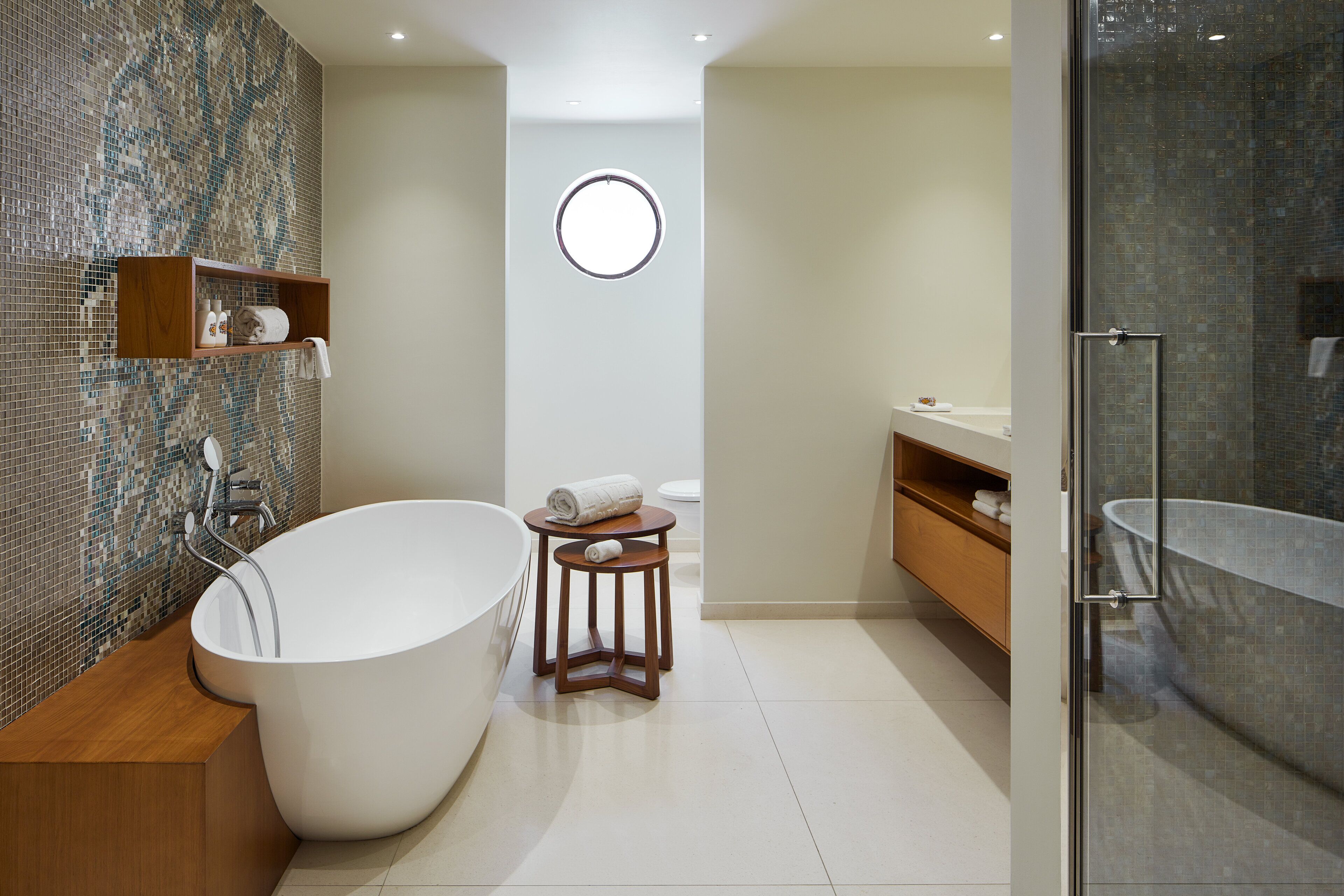 Un baño moderno con una bañera independiente, un ventanal redondo y una zona de ducha con cerramientos de vidrio.