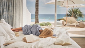 A room with a bed, a window with curtains, a view of the ocean, and a lounge area with chairs and an umbrella. - Vila Vita Parc  (Lagoa)