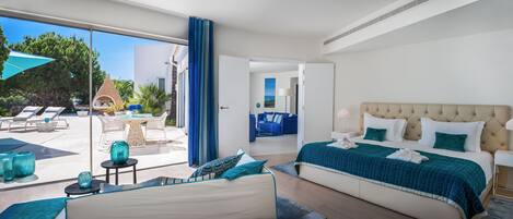 A modern hotel room with a large bed, a balcony with lounge chairs, and a view of the outdoors.