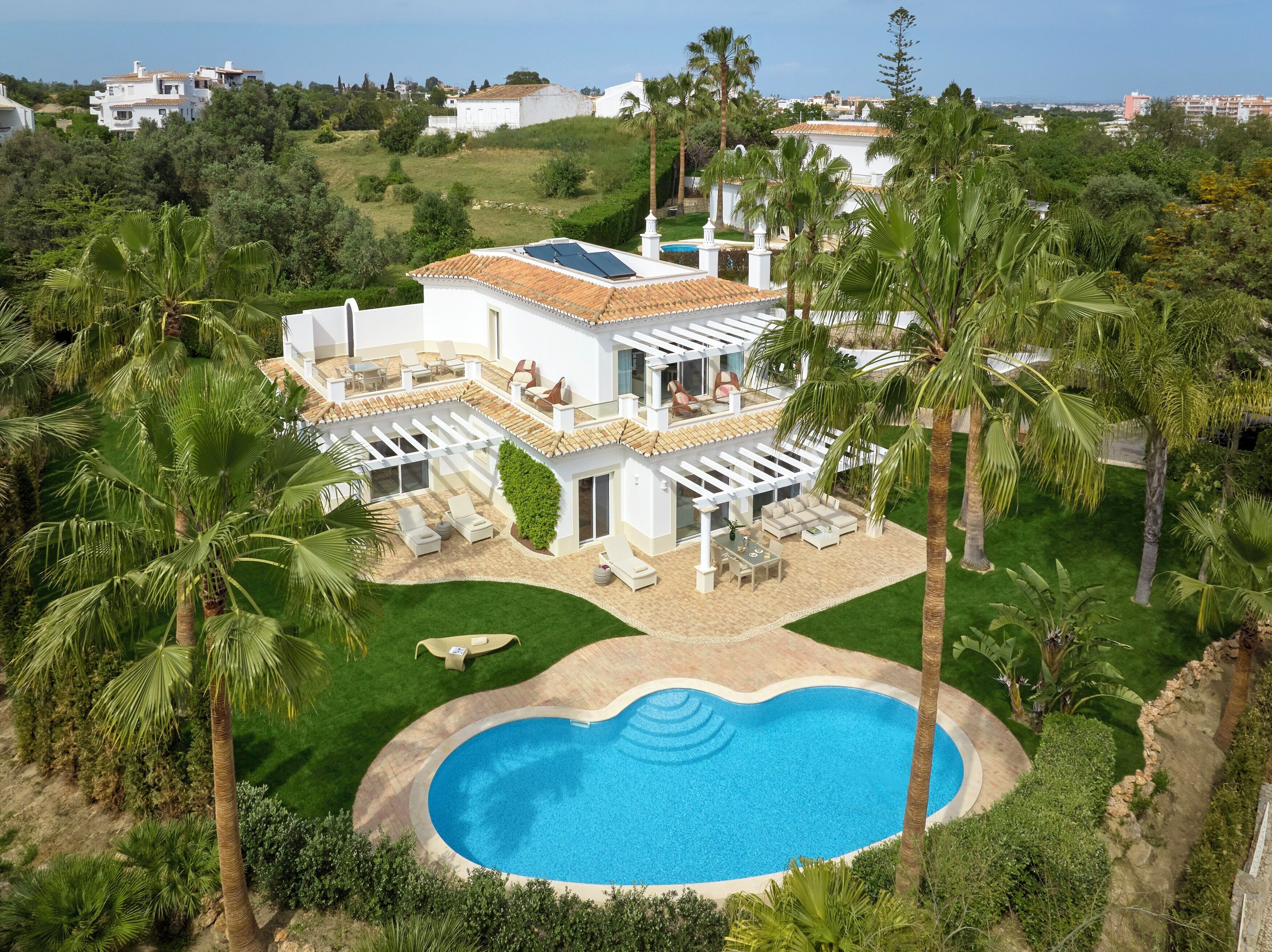 A two-story house with a swimming pool, surrounded by palm trees and a well-maintained lawn.