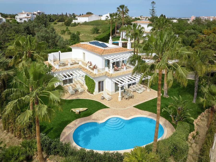 A two-story house with a swimming pool, surrounded by palm trees and a well-maintained lawn.
