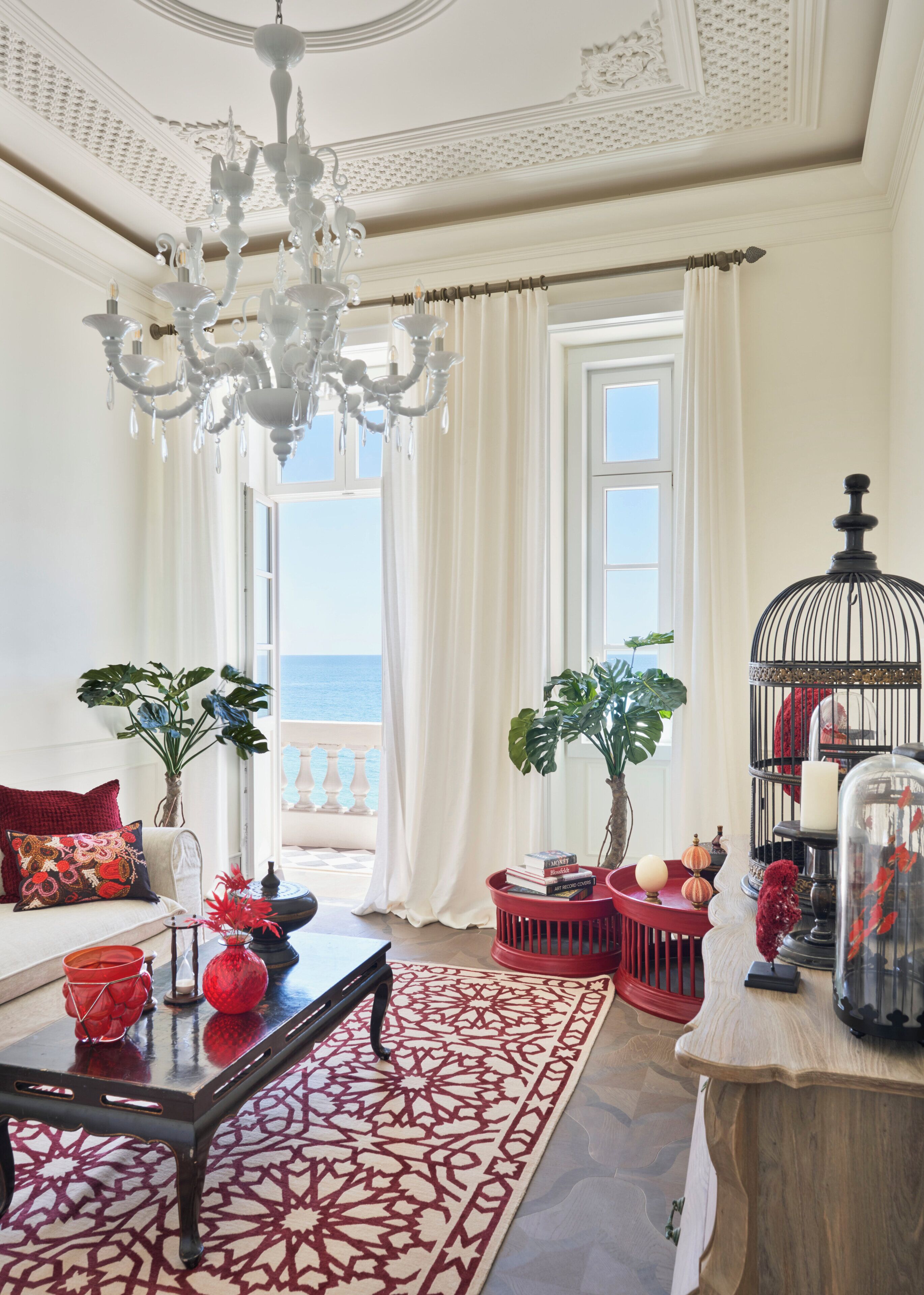 Ein großzügiges Wohnzimmer mit einer üppigen Kandelaber, einem roten Teppich mit Muster und Meerblick durch große Fenster.