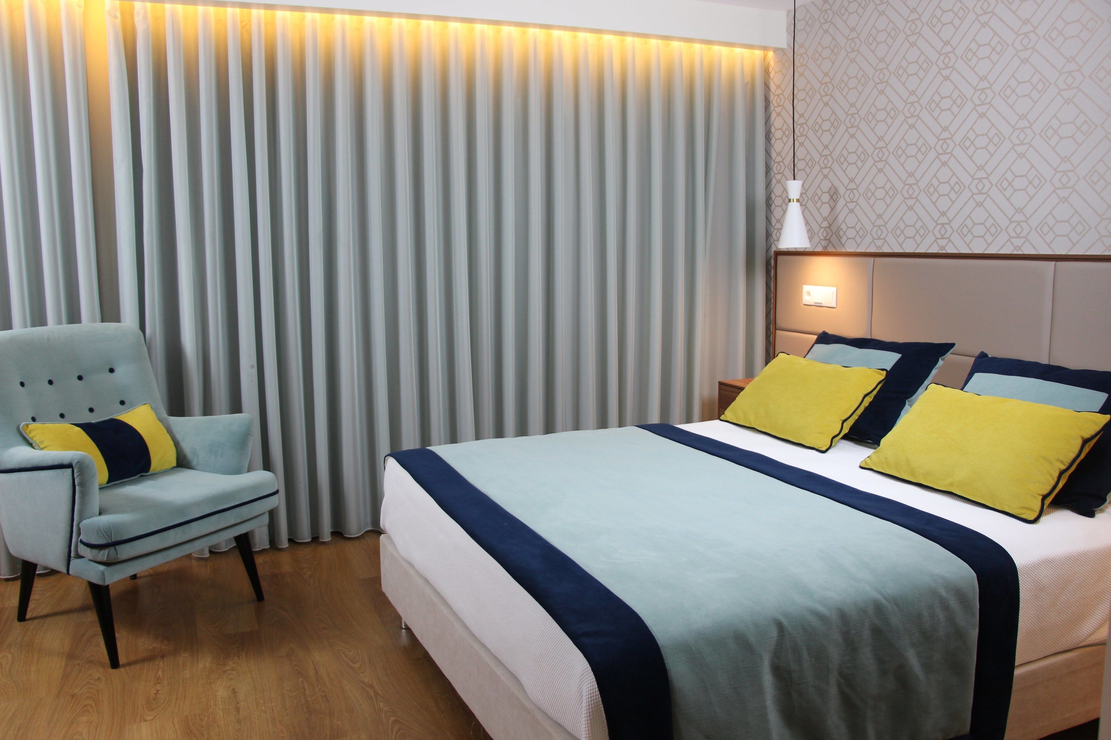 Een hotelkamer met een bed, een stoel, een gordijn en een muur met een geometrisch patroon.