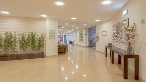 A modern hotel lobby with a glass wall, a reception desk, and a mirror with decorative plants. - Hotel Cinquentenário & Conference Center (Ourem)