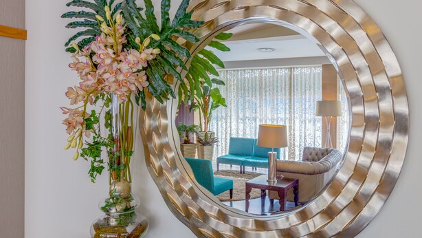 A living room with a large mirror, a teal armchair, a grey sofa, and a decorative plant arrangement. - Hotel Cinquentenário & Conference Center (Ourem)