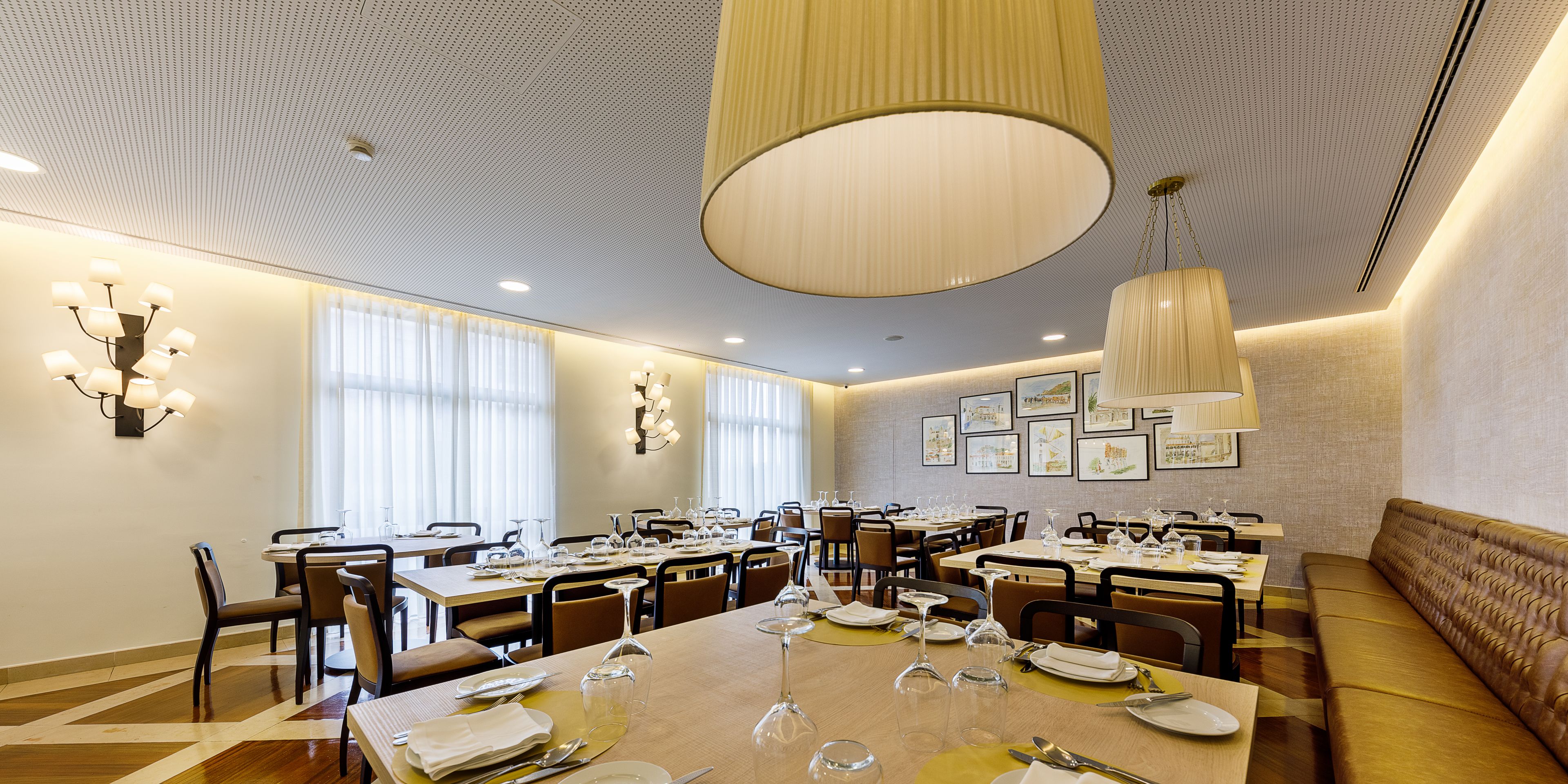 Un comedor espacioso con varias mesas dispuestas para comer, ventanas amplias y un techo alto con una lámpara central.