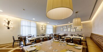 Un comedor espacioso con varias mesas dispuestas para comer, ventanas amplias y un techo alto con una lámpara central.