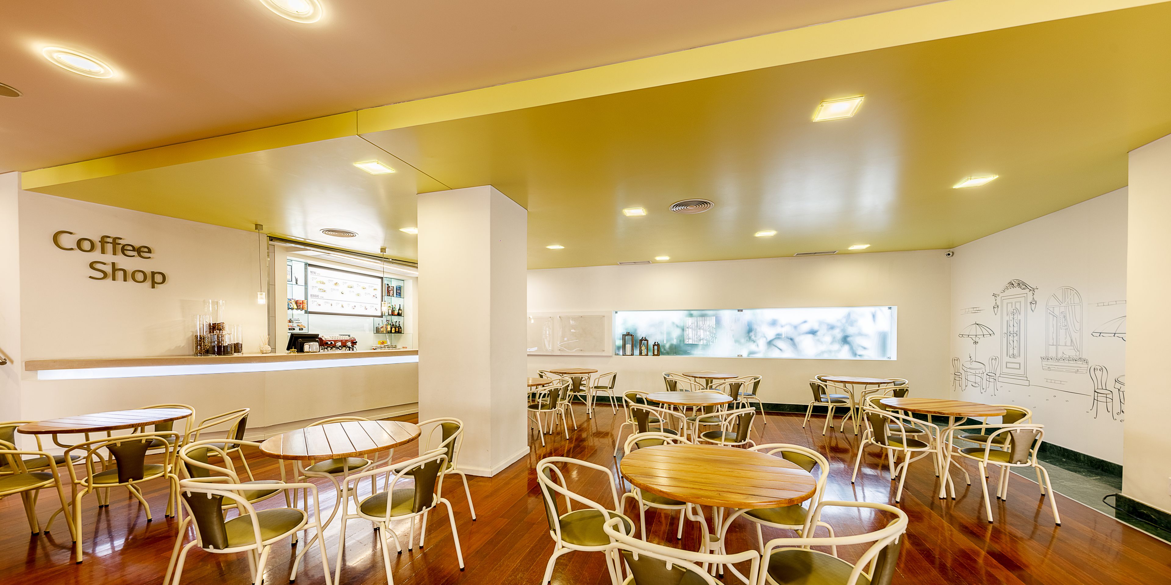 A coffee shop interior with multiple tables and chairs, a counter with a menu, and a large window with a view.