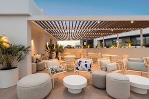 An outdoor seating area with round tables and white wicker chairs, surrounded by potted plants and a wooden pergola. - Hotel Orquidea (Funchal)