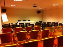 Ett konferensrum med rader av stolar, ett bord med ett vitt bordsduksöverdrag och en projektor i taket.