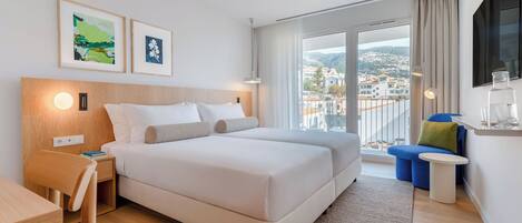 A hotel room with a bed, a desk, a chair, a small table, and a TV.