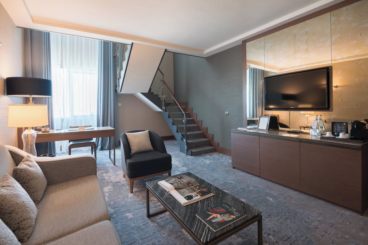 A modern hotel room with a sofa, coffee table, TV, and a staircase.