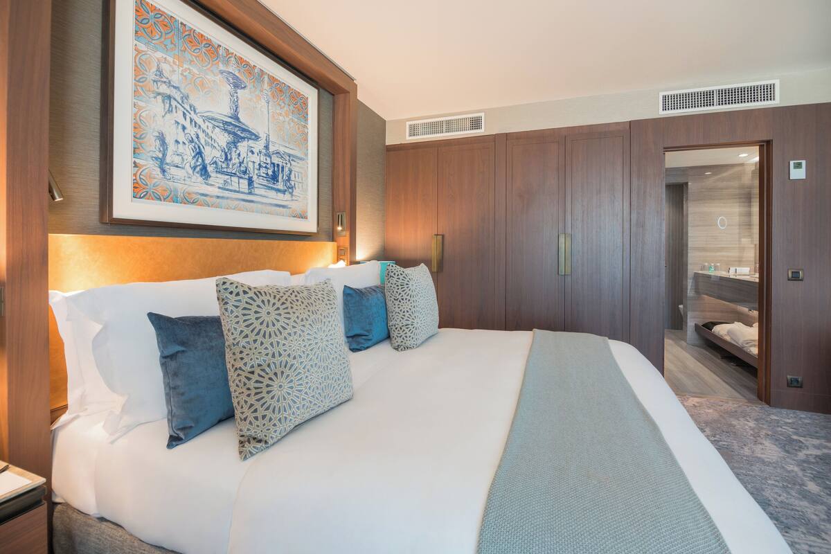 A hotel room with a large bed, a wardrobe, and a framed artwork on the wall.