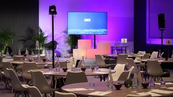A conference room with tables and chairs, a large screen displaying 'LUNCH', and a stage with a podium.