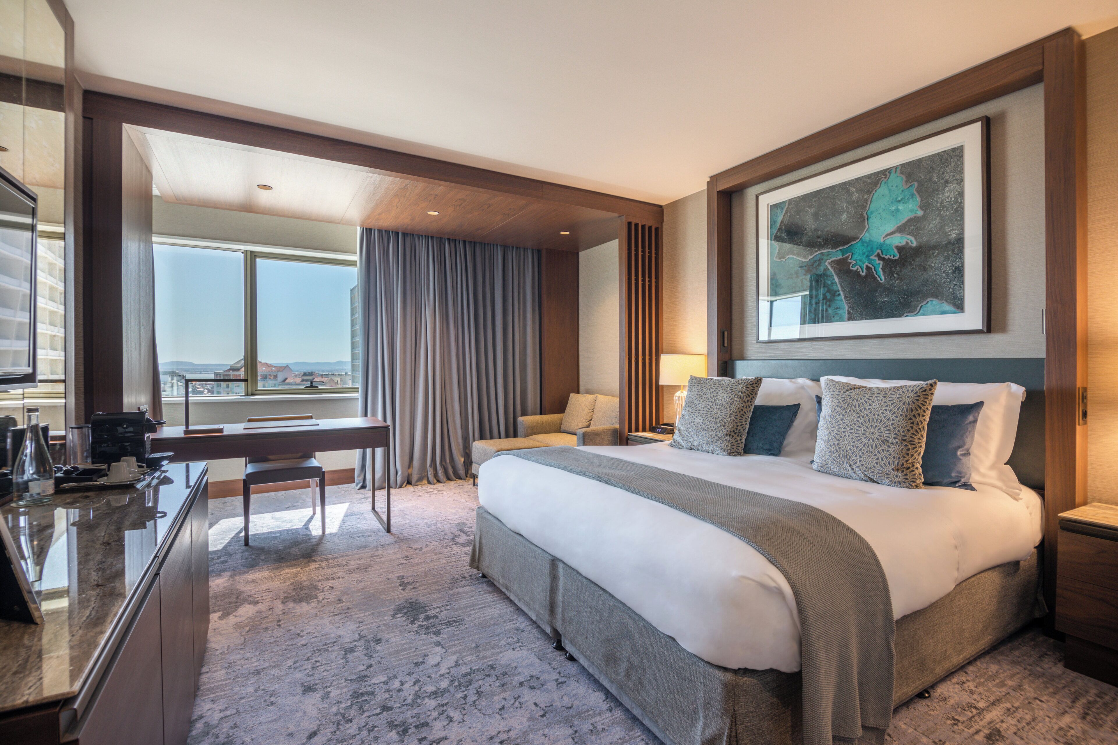 A hotel room with a large bed, a desk, and a view of the city.