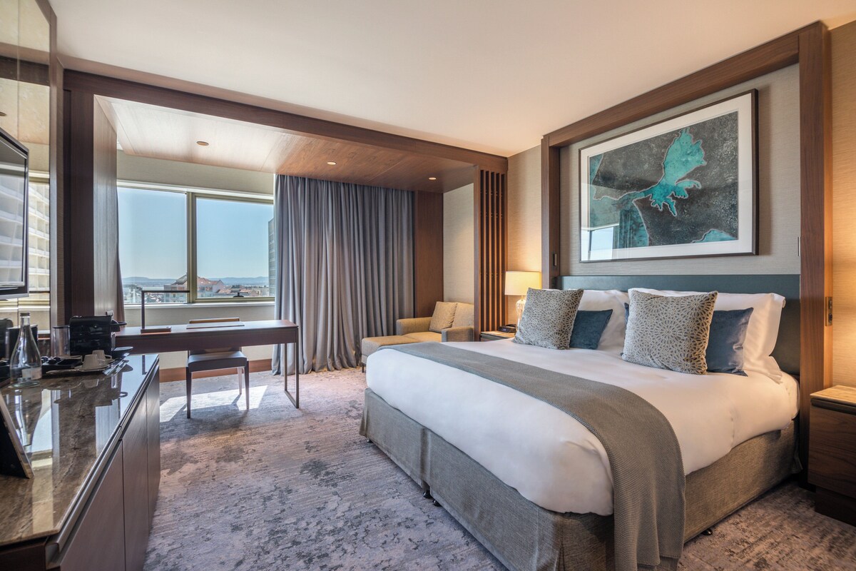 A hotel room with a large bed, a desk, and a view of the city.